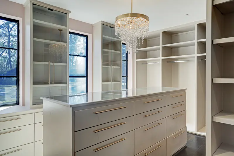 Primary closet with center island, open shelving and crystal chandelier