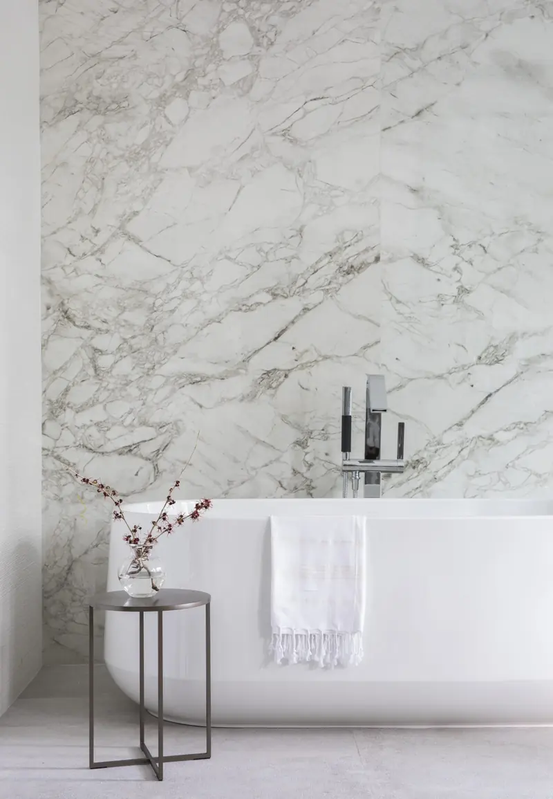 Freestanding tub against a full-height marble slab wall