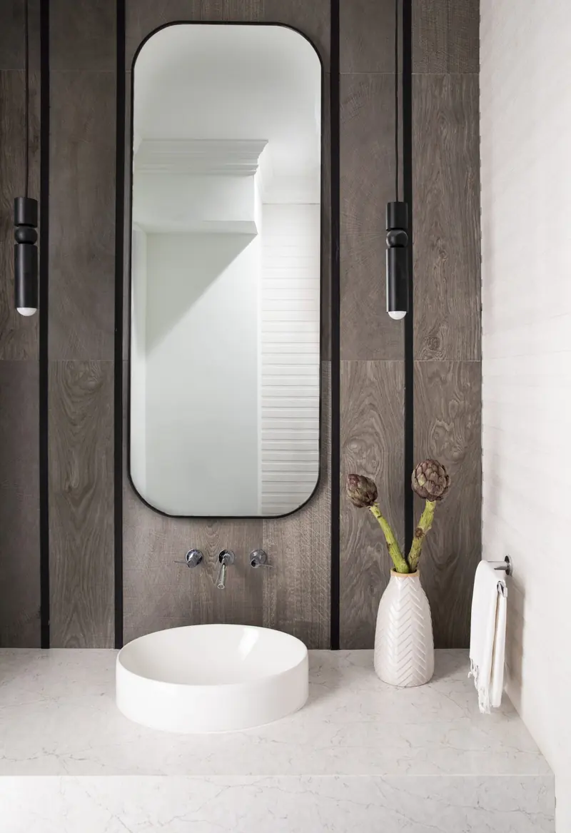 Powder room with wood-paneled wall, oval mirror and vessel sink